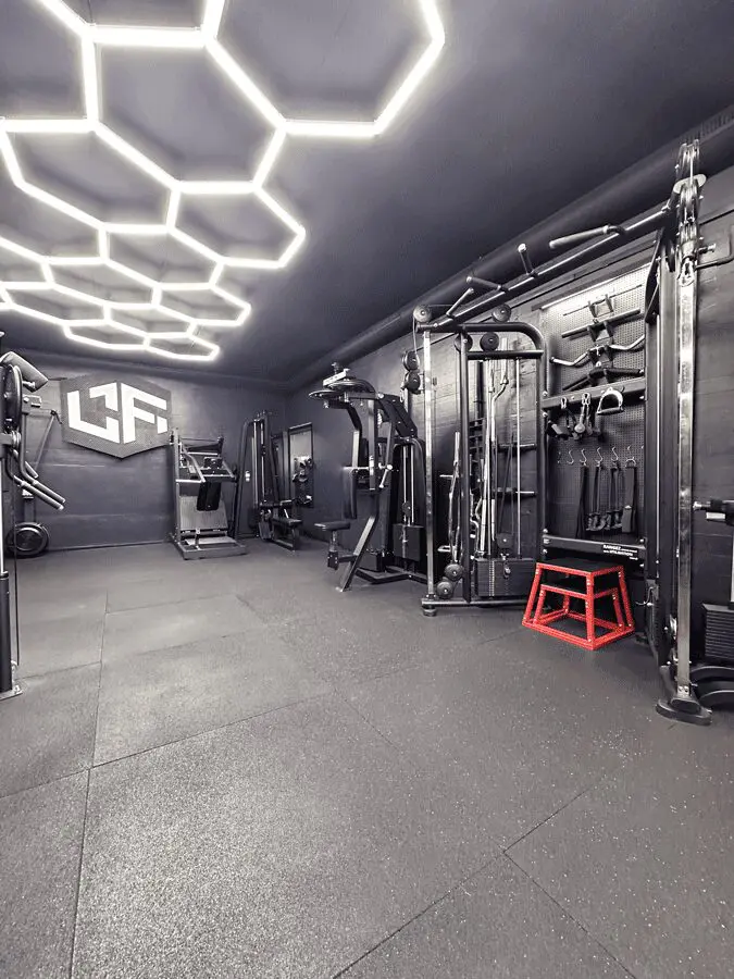 Zone d'entraînement fonctionnel à La Forge Gym Neuchâtel, avec machine à poulies, logo au mur et éclairage hexagonal.