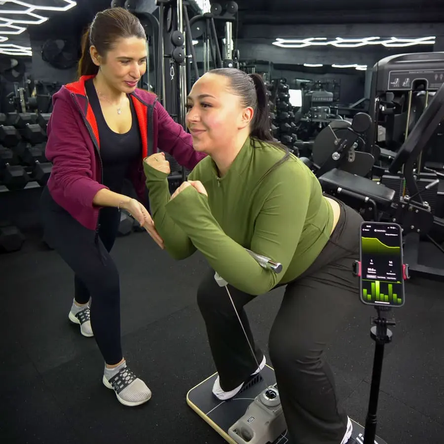 Coach de La Forge One Fitness guidant une cliente lors d'un entraînement de renforcement musculaire avec capteurs de performance.